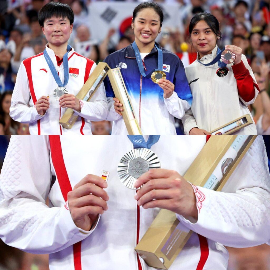 Die chinesische Badmintonspielerin He Bingjiao trägt ein spanisches Flaggenabzeichen auf das Podium, nachdem ihre spanische Halbfinalgegnerin verletzungsbedingt zurückgetreten war