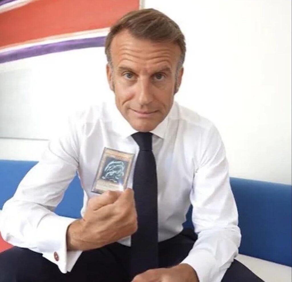 Macron hält eine blaue Augen weiße Drachenkarte hoch