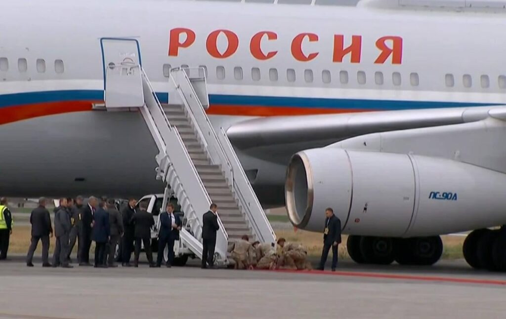 Amerikanische Soldaten knien knien, um einen roten Teppich in den Stufen von Putins Flugzeug auszuwirken, beobachtet von Putins Sicherheitskräften