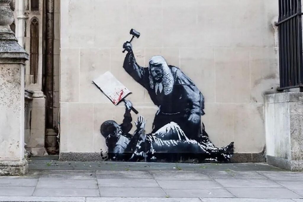 Banksy zeigte einen Richter, der seinen Hammer über einen gefallenen Demonstranten erhöhte. Graffiti an den königlichen Gerichten war mit Plastik und Barrieren bedeckt Banksy zeigte einen Richter, der seinen Hammer über einen gefallenen Demonstranten erhöhte. Graffiti an den königlichen Gerichten war mit Plastik und Barrieren bedeckt