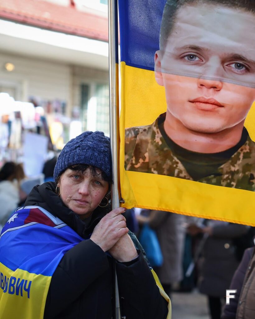 Am 1571. Tag der groß angelegten Invasion ist die Sonne über Kiew untergegangen. Frau hält beim Kriegsgefangenenaustausch ein Schild für einen ukrainischen Soldaten, dessen Schicksal unbekannt ist